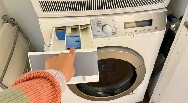 Mano indica il cassetto della lavatrice, dove si mette il detersivo. Forse l'ammorbidente fa male ai tessuti, meglio evitare.