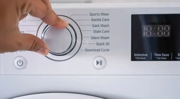 Mano che gira la manopola della lavatrice per scegliere il programma. La lavatrice usa acqua calda o fredda a seconda del ciclo selezionato.