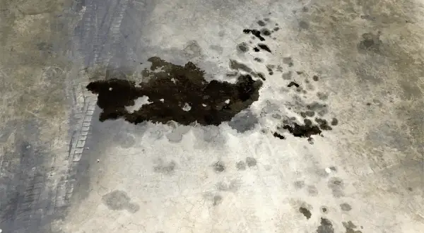 Macchie scure di grasso meccanico sul cemento, con tracce di pneumatici. Un problema comune da risolvere per chi lavora con i motori.
