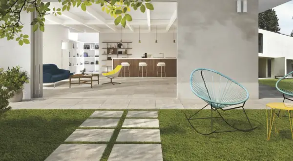 Modern patio with stone pavers, grass, and outdoor seating, opening to a bright, open-plan living and kitchen area.