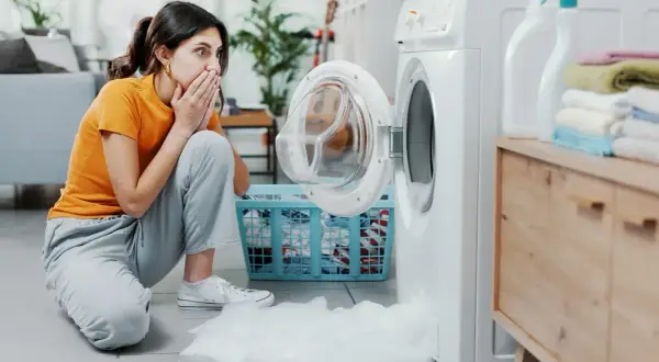 Donna sorpresa con le mani sulla bocca, la lavatrice perde schiuma. Scopri come eliminare la schiuma dalla lavatrice.
