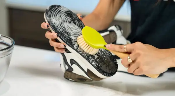 Mani che puliscono la suola di una scarpa con una spazzola, mostrando come pulire le scarpe senza lavarle.