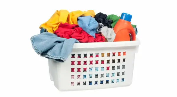 Cesto bianco pieno di panni colorati, con una bottiglia di detersivo arancione. Pronto per il bucato con perborato di sodio.