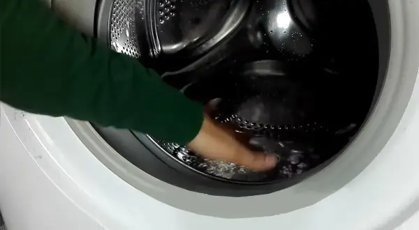 Mano che tocca l'acqua residua nel cestello della lavatrice, un passo per capire come togliere l'acqua dalla lavatrice.
