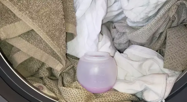 Un cestello pieno di biancheria, con un misurino di ammorbidente rosa. Si può mettere l'ammorbidente direttamente nel cestello per un bucato profumato.