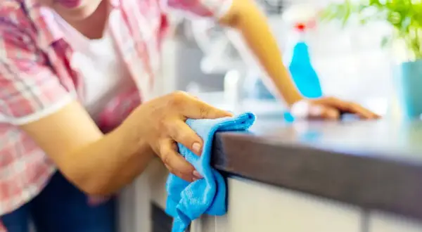 Donna pulisce il piano della cucina con un panno blu, un metodo efficace per sgrassare la cucina e mantenerla splendente.