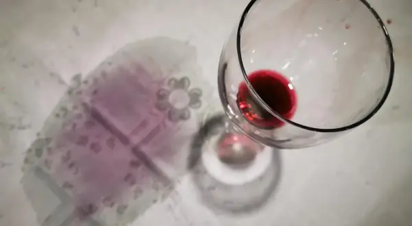 Un bicchiere rovesciato ha lasciato macchie di vino rosso sui capi colorati di una tovaglia.