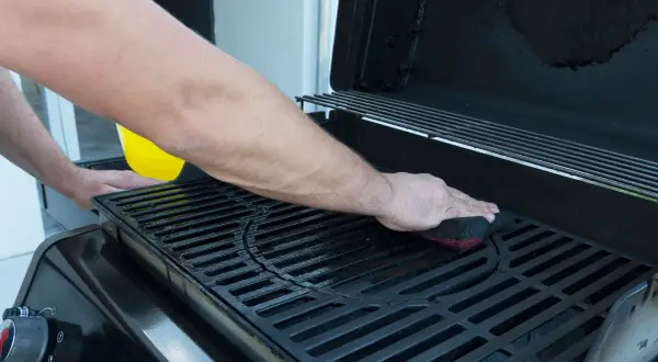 Uomo pulisce la griglia della barbecue con una spugna. Un liquido giallo viene versato da un contenitore.