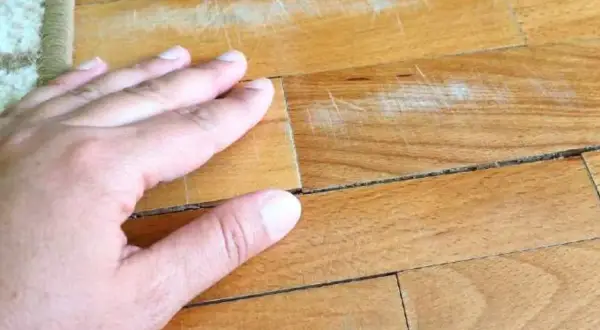 Mano sul parquet con macchie vecchie di olio e graffi evidenti.