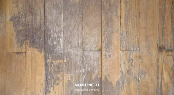 Parquet rovinato dall'acqua, con doghe in legno che mostrano macchie scure e usura, testimoni di un passato umido.