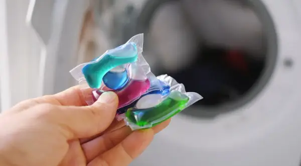 Mani che tengono capsule colorate per lavatrice. Attenzione, le capsule rovinano la lavatrice se usate impropriamente.