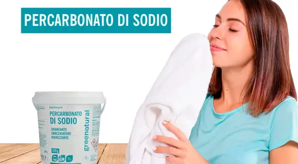 Donna annusa un asciugamano bianco fresco, accanto a un contenitore di percarbonato di sodio. Il percarbonato si può usare sui colorati per un bucato impeccabile.