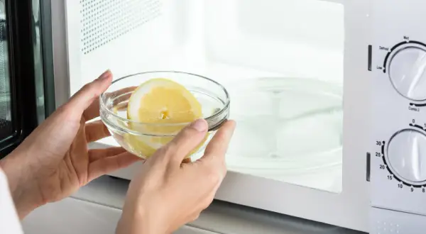Mani inseriscono una ciotola con acqua e limone nel microonde, un metodo semplice per pulire l'elettrodomestico.