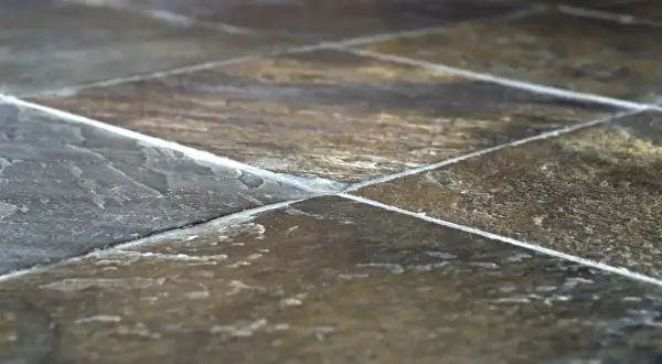 Primo piano di una pavimentazione in pietra di lavagna, con le sue venature naturali e le fughe bianche che creano un motivo geometrico.