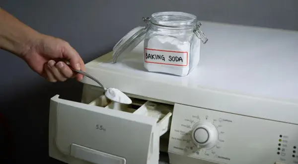 Mano aggiunge bicarbonato di sodio, un ingrediente naturale per la soda per lavatrice, nel cassetto del detersivo.