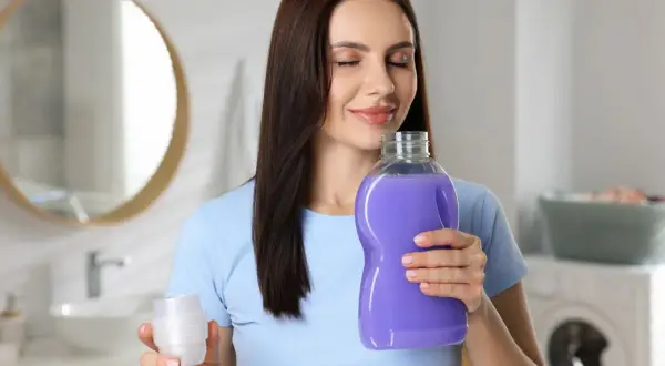 Donna annusa una bottiglia di ammorbidente viola, godendosi il profumo. Scopri come profumare la casa con l'ammorbidente.