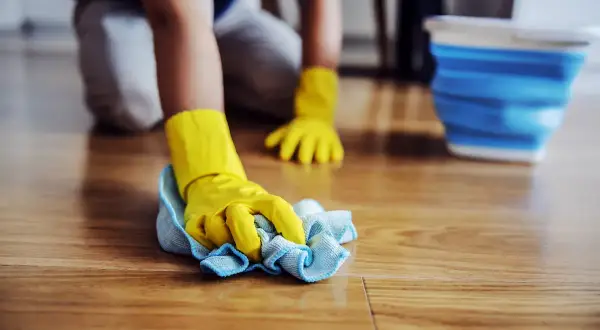 Mani con guanti gialli puliscono il pavimento in legno, rimuovendo la muffa con un panno.