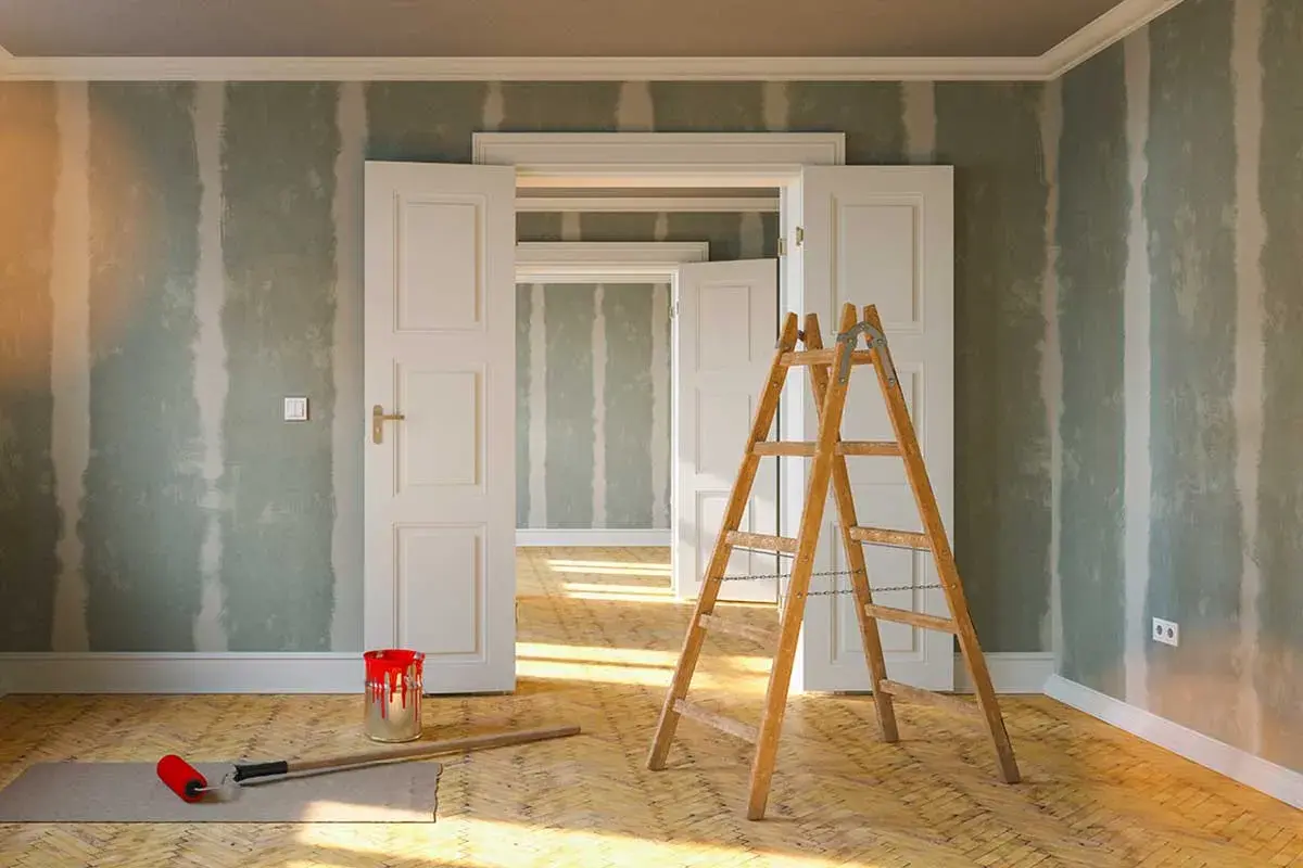 Rullo, secchio di vernice rossa e scala in legno pronti per togliere macchie di vernice secca dalle pareti di una stanza in ristrutturazione.