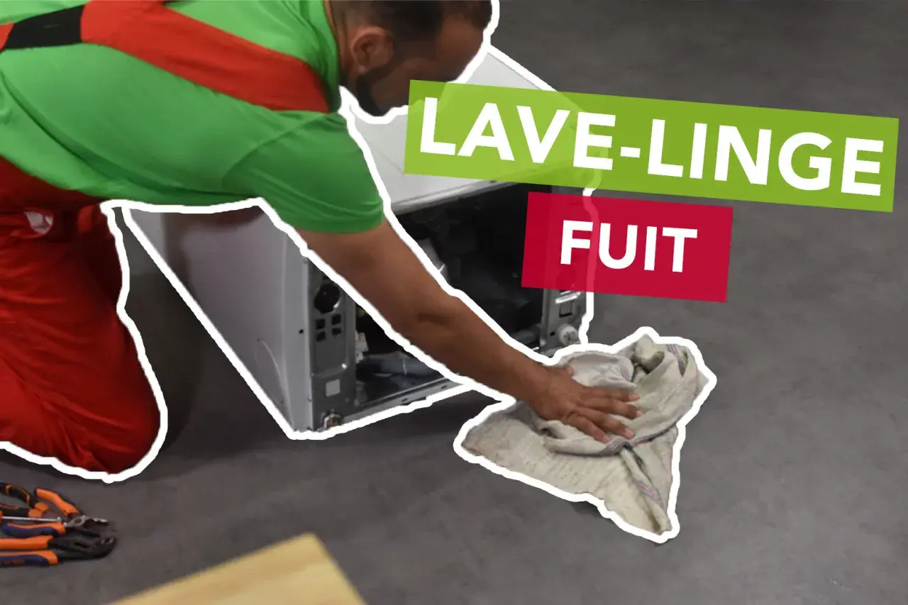 Un tecnico con tuta rossa e verde asciuga con uno straccio il pavimento dove la lavatrice perde acqua dal cestello.