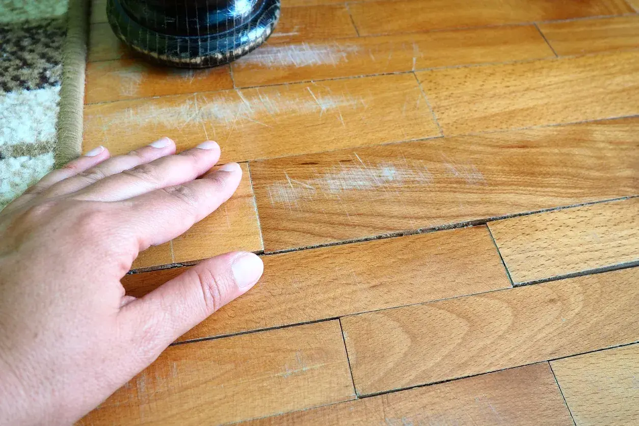 Mano su parquet graffiato, pronto per essere pulito con aceto e bicarbonato per un restauro fai-da-te.