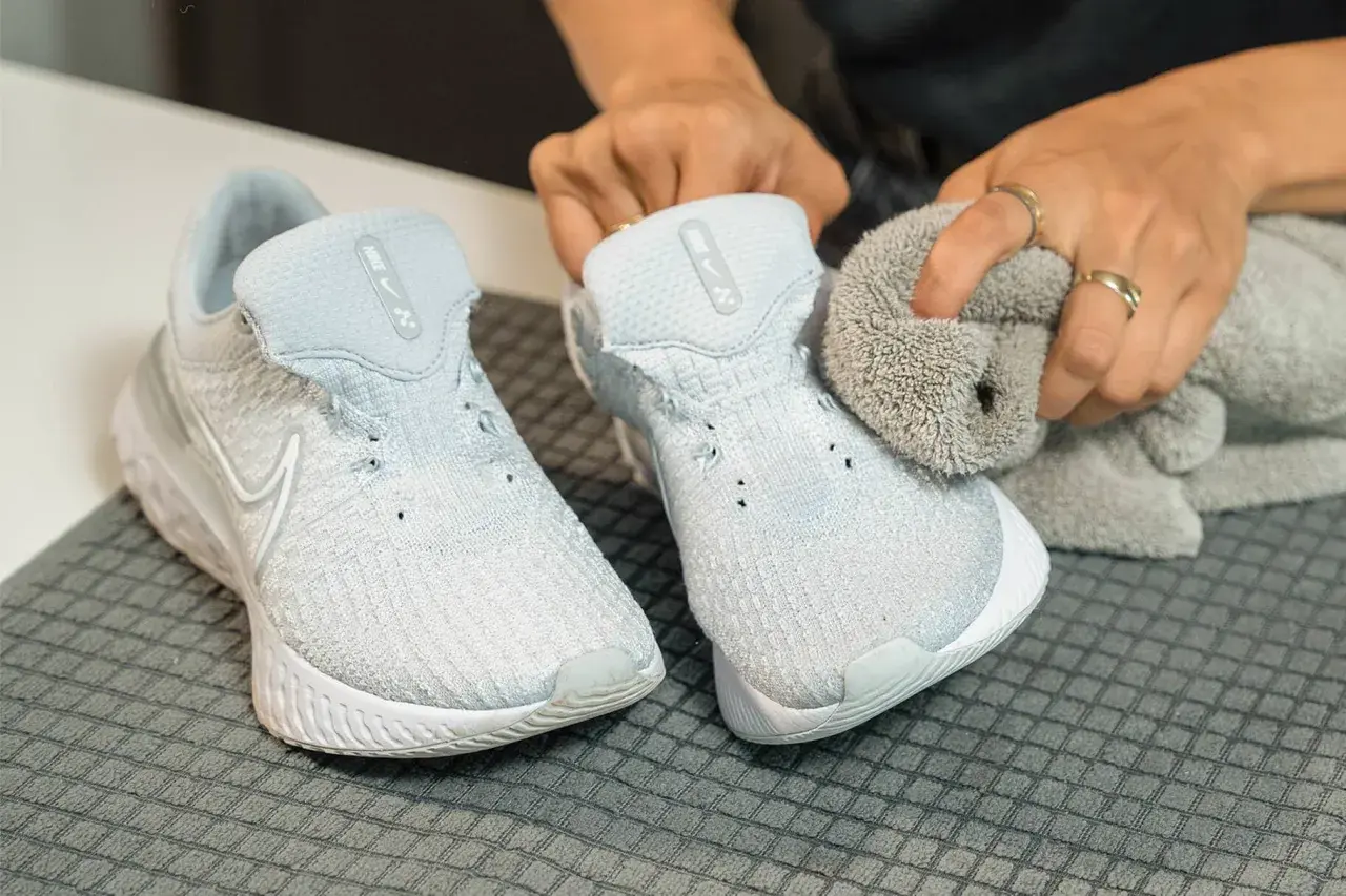 Hands cleaning light blue Nike sneakers with a grey cloth.
