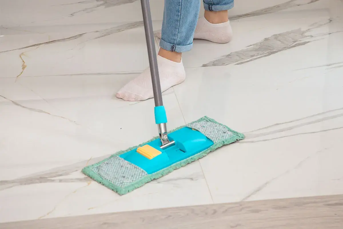 Piedi in calzini bianchi puliscono un pavimento in marmo con uno straccio blu e verde. Ecco come pulire il marmo per farlo brillare.