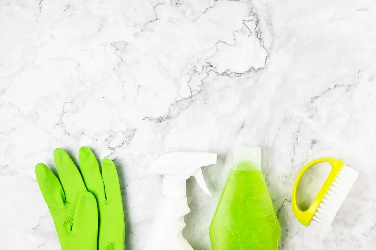 Guanti verdi, spray bianco, flacone di liquido verde e spazzola gialla pronti per scoprire come pulire pietra.