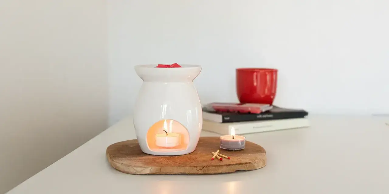Diffusore bianco con candela accesa e cubetti di cera profumata sopra. Un'altra candela e fiammiferi completano la scena, mostrando che cos'è la cera per profumare l'ambiente.