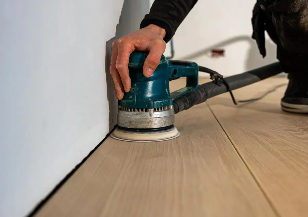 Mano che usa una levigatrice per levigare parquet a mano, creando una superficie liscia e pronta per la finitura.