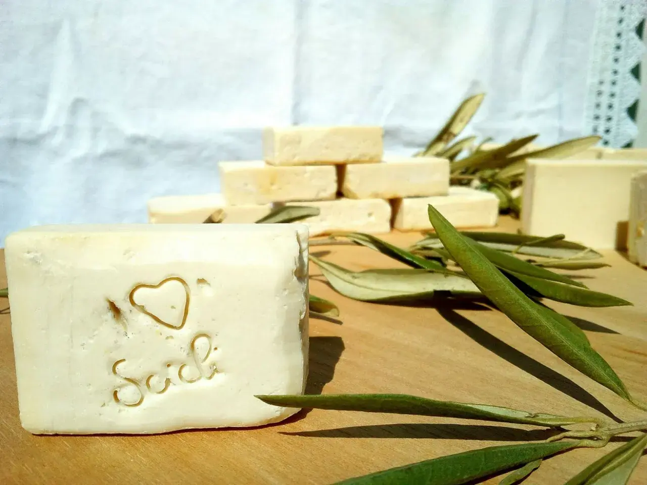 Sapone artigianale, frutto della saponificazione olio di oliva, con decorazione a cuore e scritta "Sich". Foglie d'ulivo completano la scena.