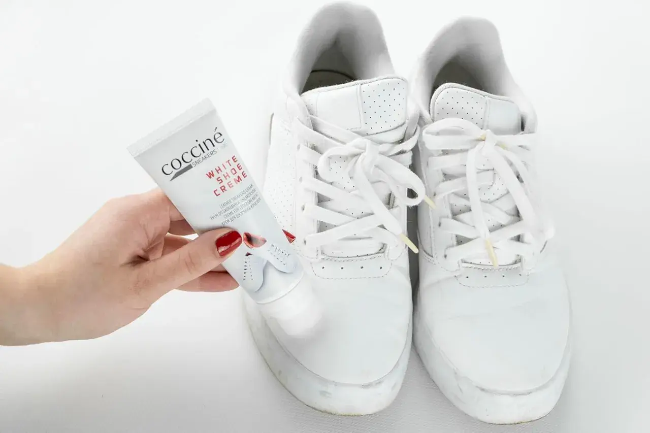 Mano con tubetto di crema per scarpe bianche, pronto a pulire le sneakers. Un metodo efficace per far tornare come nuove le tue scarpe bianche.
