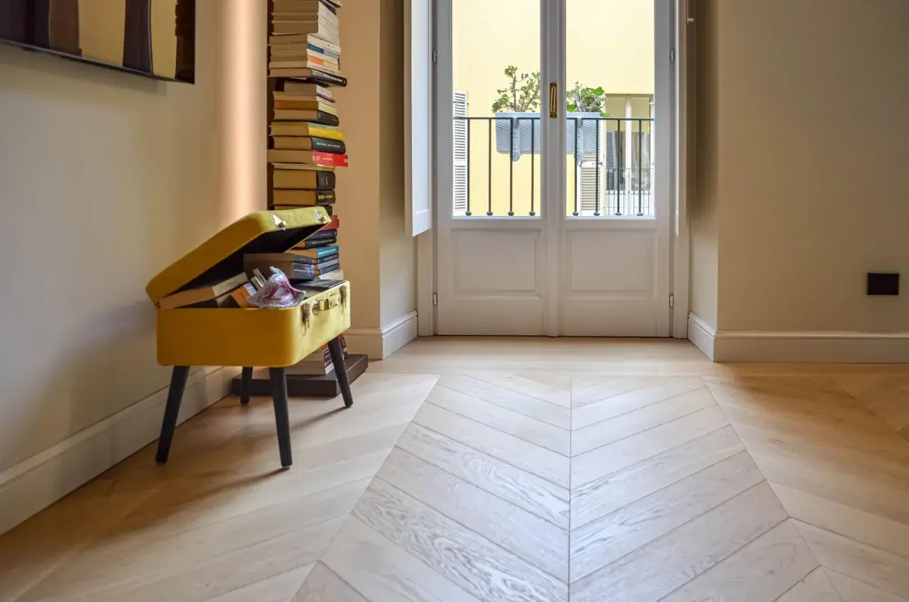 Un elegante parquet a spina di pesce, con finitura opaca, riflette la luce che entra dalla porta-finestra.
