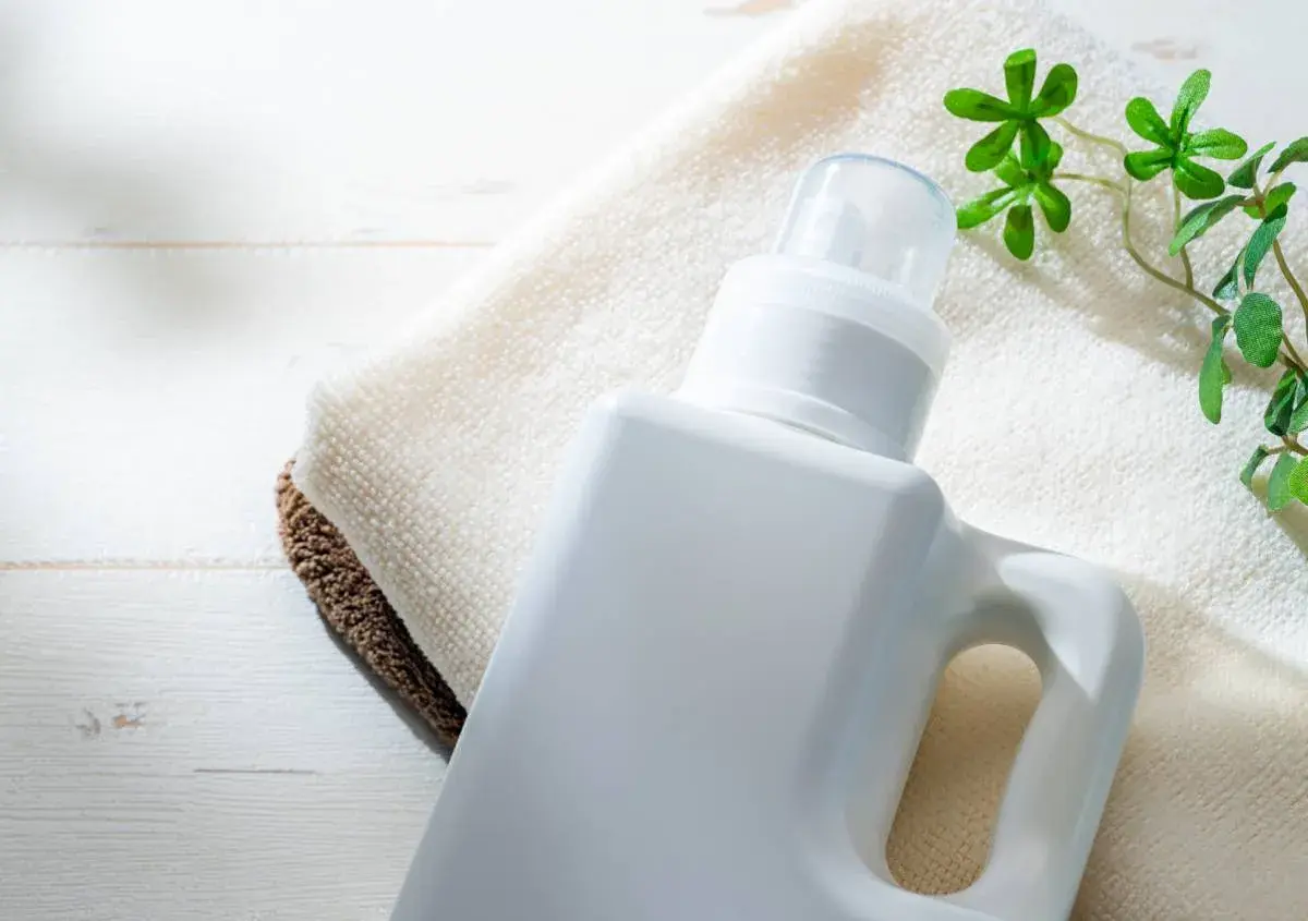 Flacone bianco di detersivi ecologici altroconsumo su asciugamani, con foglioline verdi.