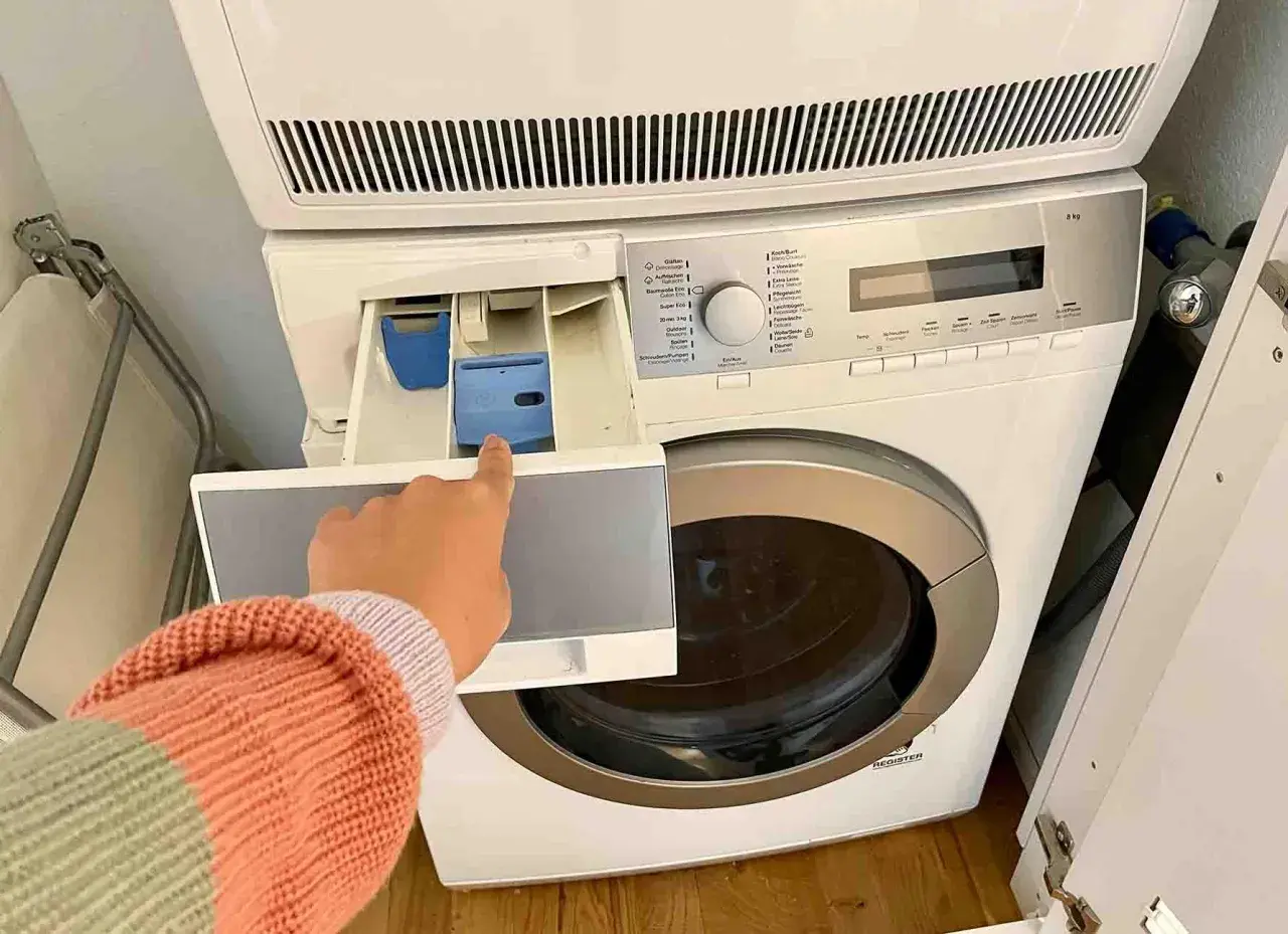 Mano indica il cassetto della lavatrice, dove si mette il detersivo. Forse l'ammorbidente fa male ai tessuti, meglio evitare.