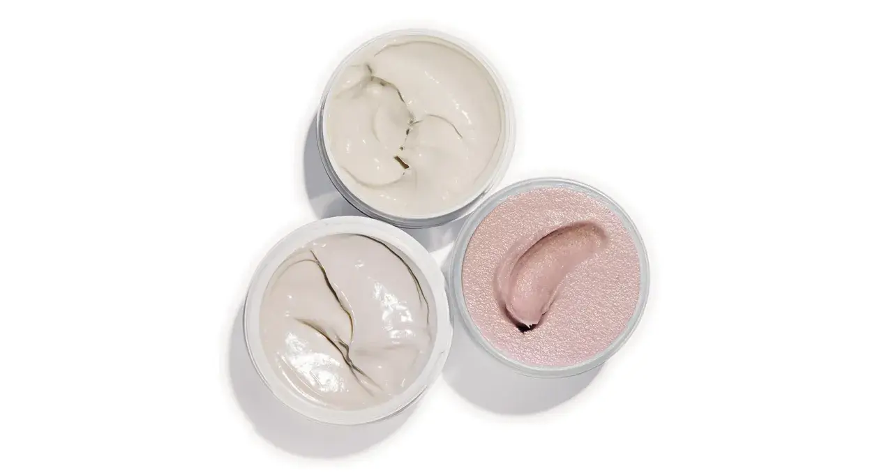 Tre barattoli aperti con texture cremose: un bianco avorio, un grigio chiaro e un rosa perlato. Ideali per un burro corpo nutriente.