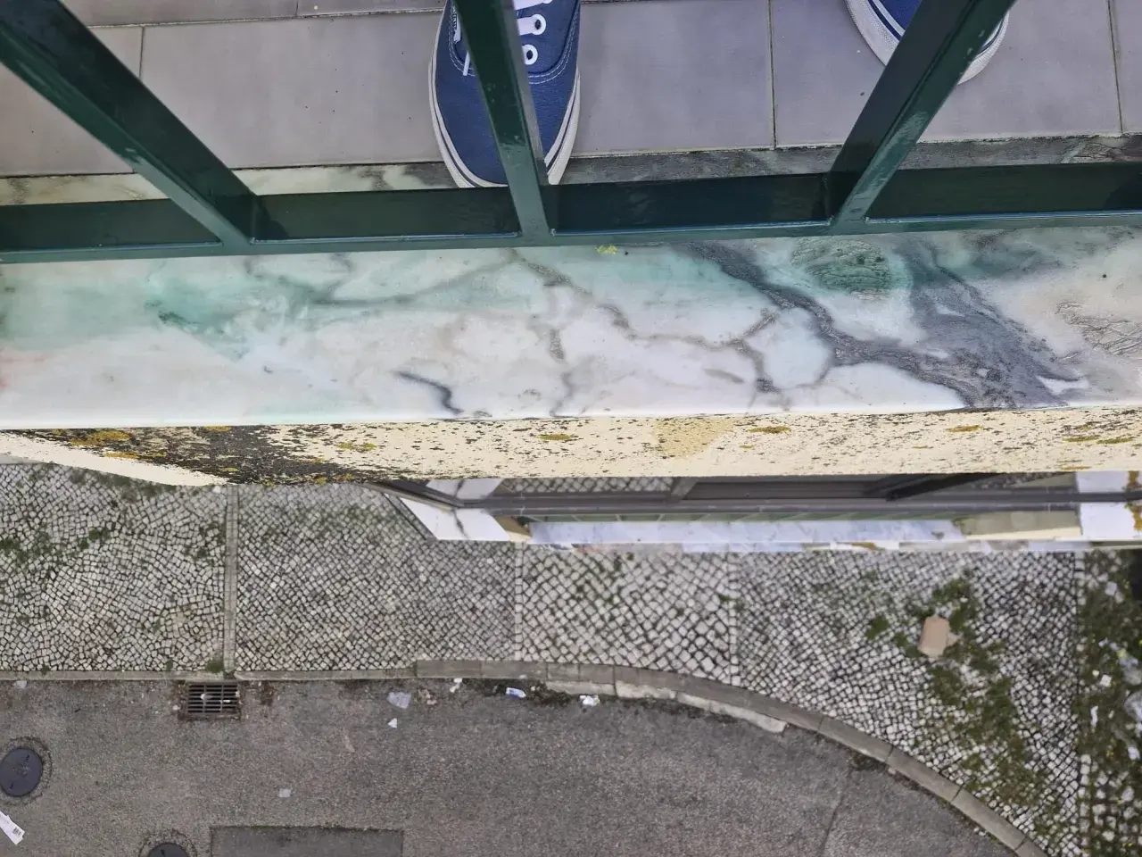 Come togliere la vernice dal marmo: una macchia verde su un davanzale di marmo, con scarpe blu in primo piano.