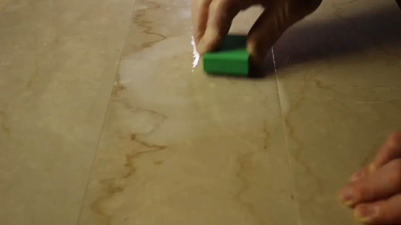 Mano che lucida un marmo corroso con una spugna verde.