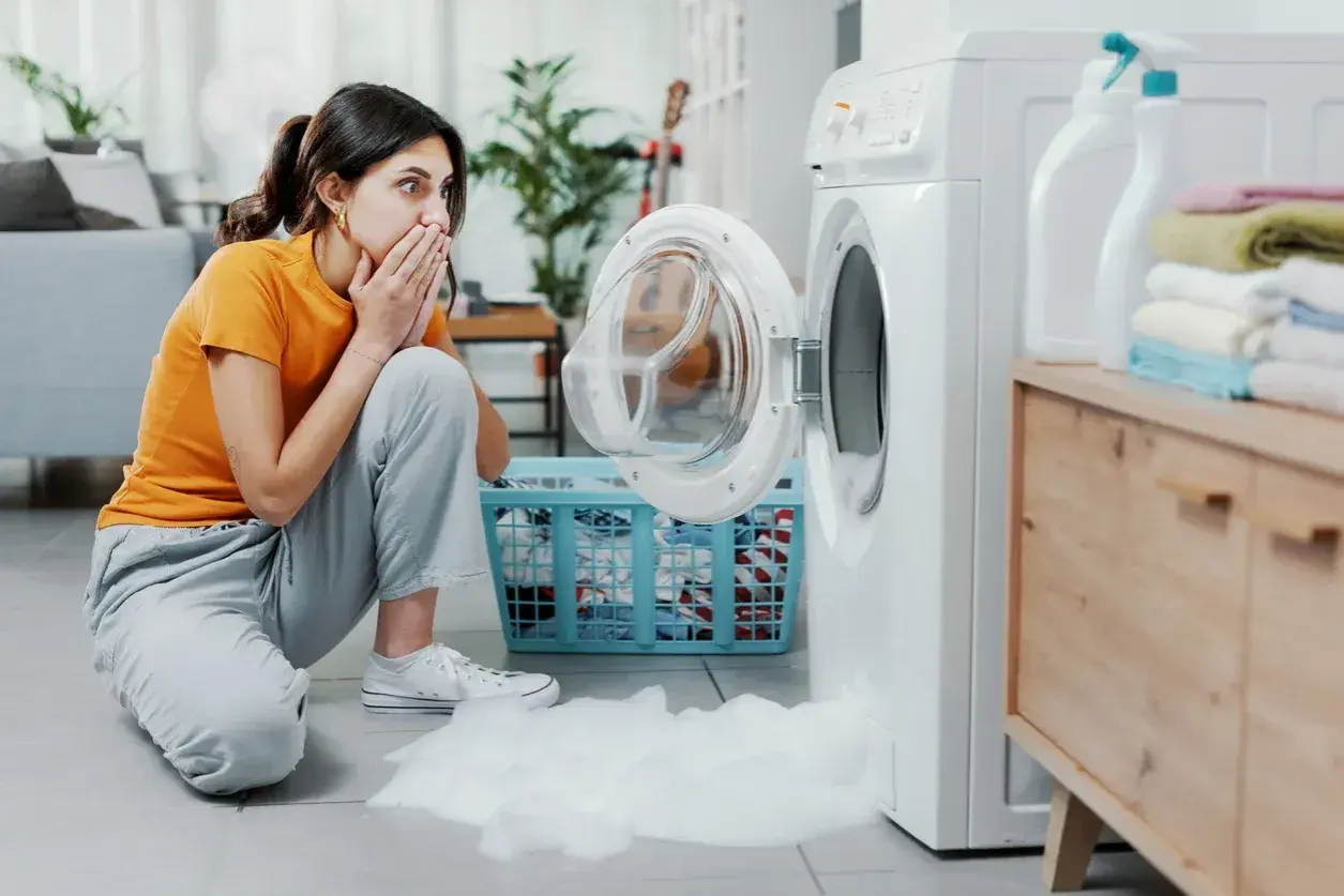 Donna sorpresa con le mani sulla bocca, la lavatrice perde schiuma. Scopri come eliminare la schiuma dalla lavatrice.
