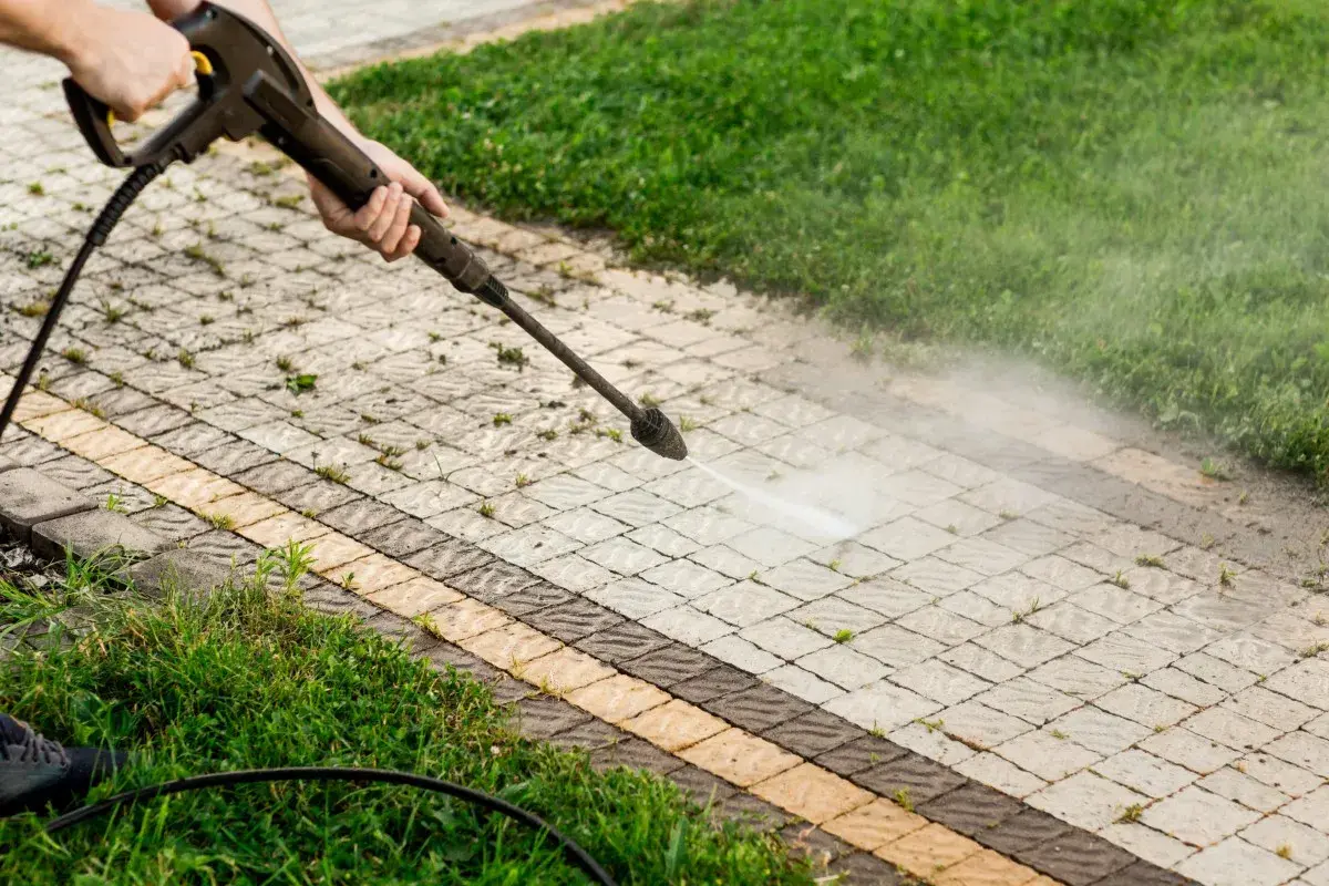 Pulizia del vialetto con idropulitrice per eliminare muschio con candeggina. L'acqua nebulizzata pulisce le fughe tra i blocchi di cemento.