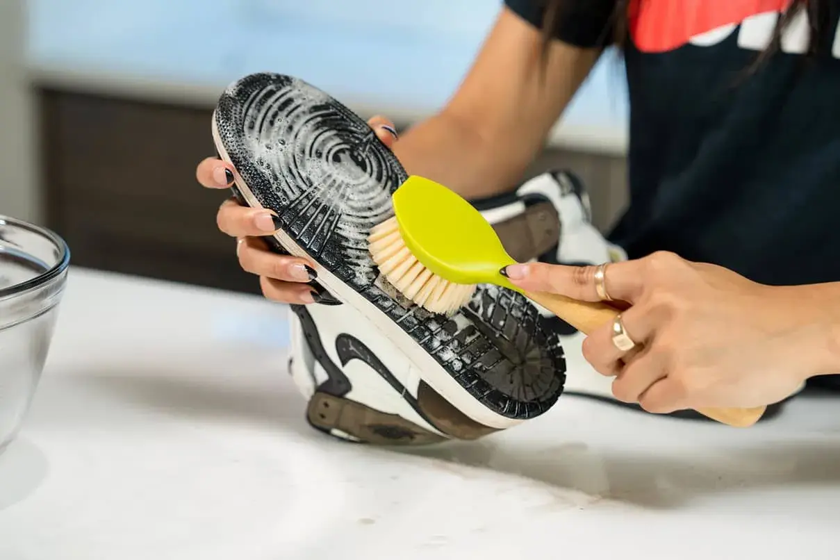 Mani che puliscono la suola di una scarpa con una spazzola, mostrando come pulire le scarpe senza lavarle.