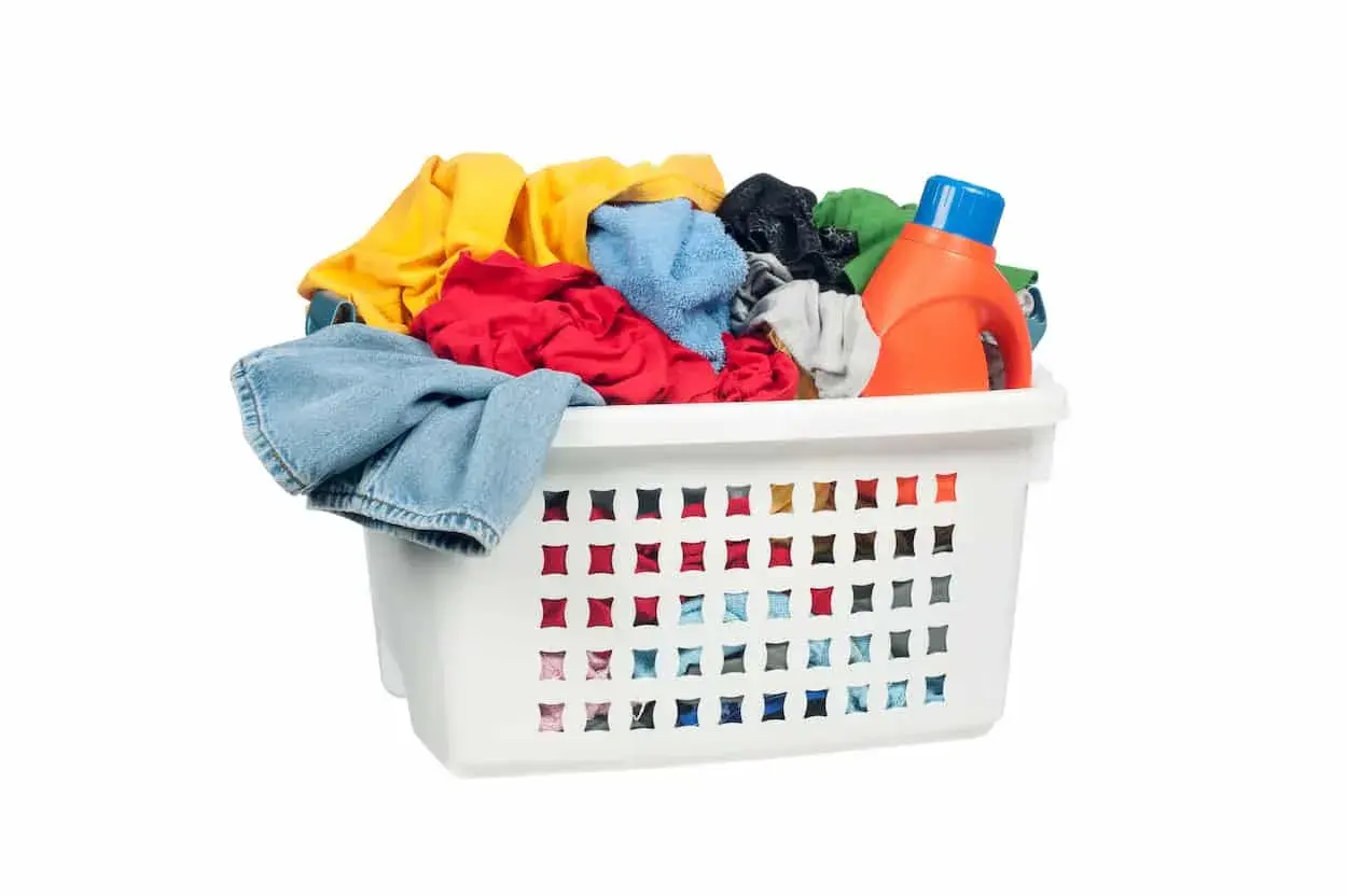 Cesto bianco pieno di panni colorati, con una bottiglia di detersivo arancione. Pronto per il bucato con perborato di sodio.