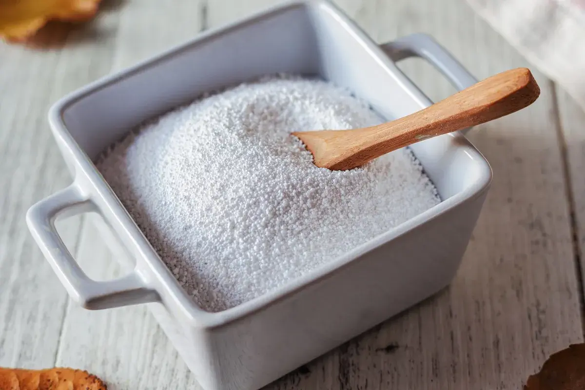 Piatto bianco con percarbonato di sodio e cucchiaio di legno. Informarsi sui percarbonato di sodio controindicazioni prima dell'uso.