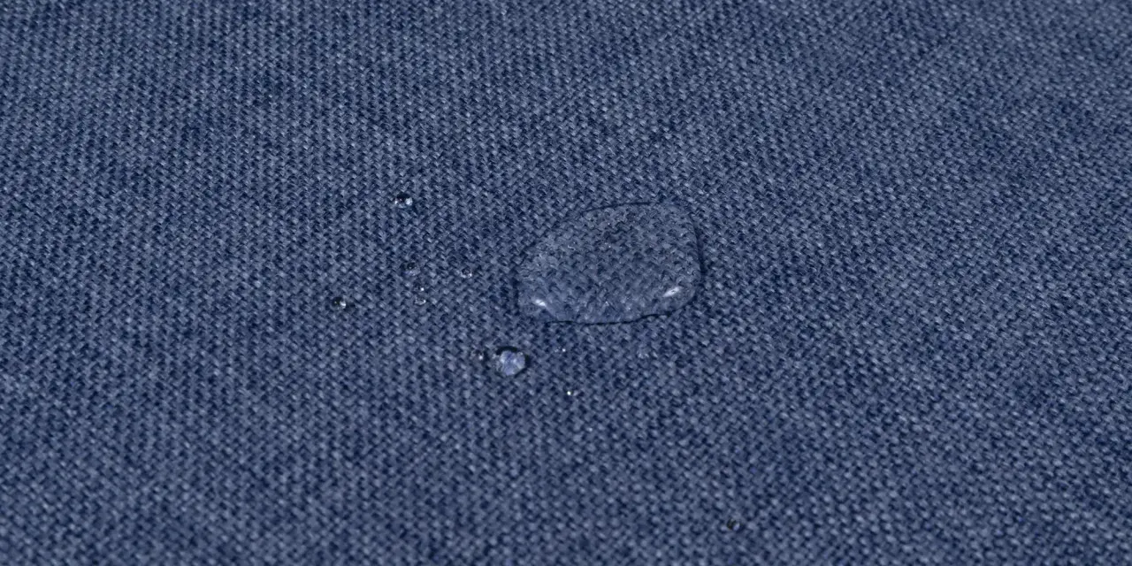 Gocce d'acqua su tessuto blu, dimostrando l'efficacia del lavaggio antimacchia in lavatrice.