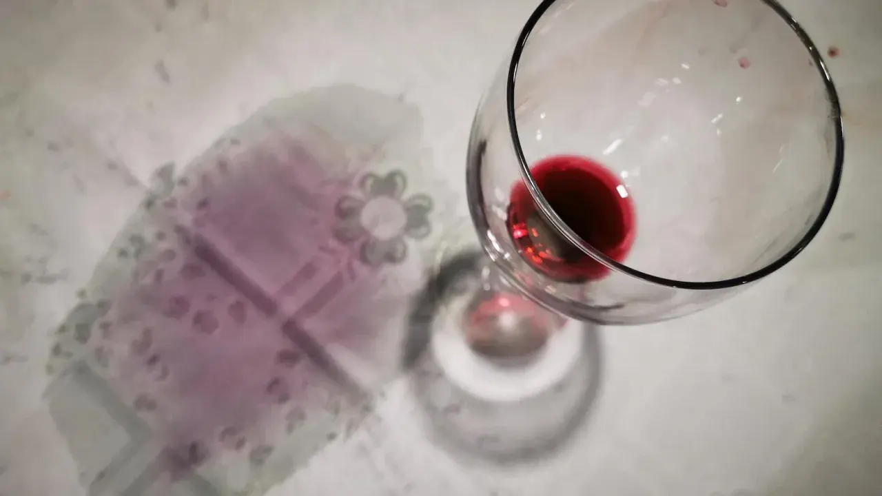 Un bicchiere rovesciato ha lasciato macchie di vino rosso sui capi colorati di una tovaglia.
