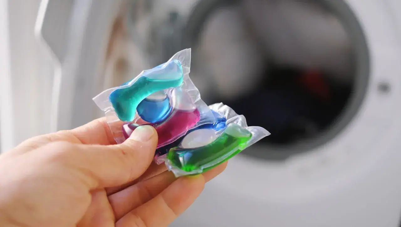 Mani che tengono capsule colorate per lavatrice. Attenzione, le capsule rovinano la lavatrice se usate impropriamente.