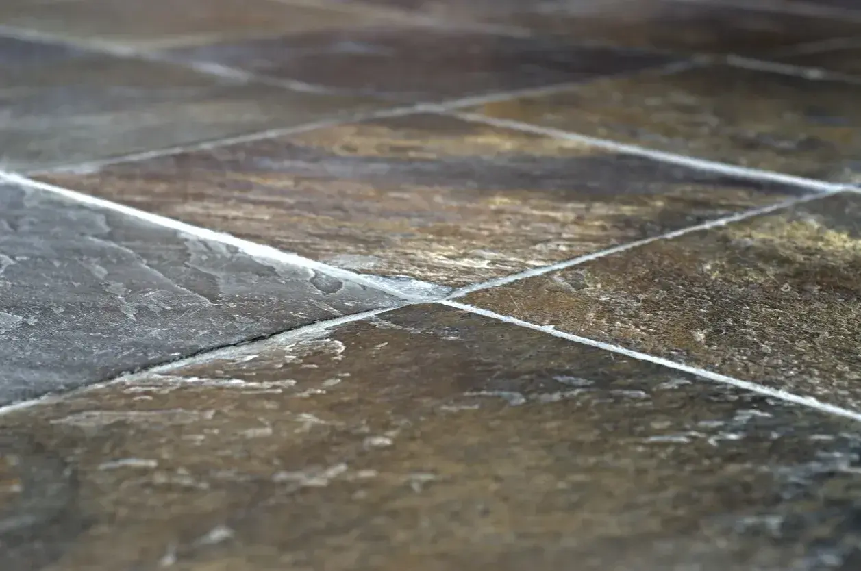 Primo piano di una pavimentazione in pietra di lavagna, con le sue venature naturali e le fughe bianche che creano un motivo geometrico.