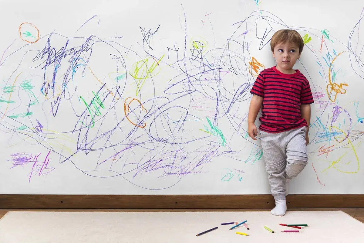 Bambino vicino a un muro pieno di scarabocchi colorati. Come togliere macchie dal muro colorato dopo il suo capolavoro.