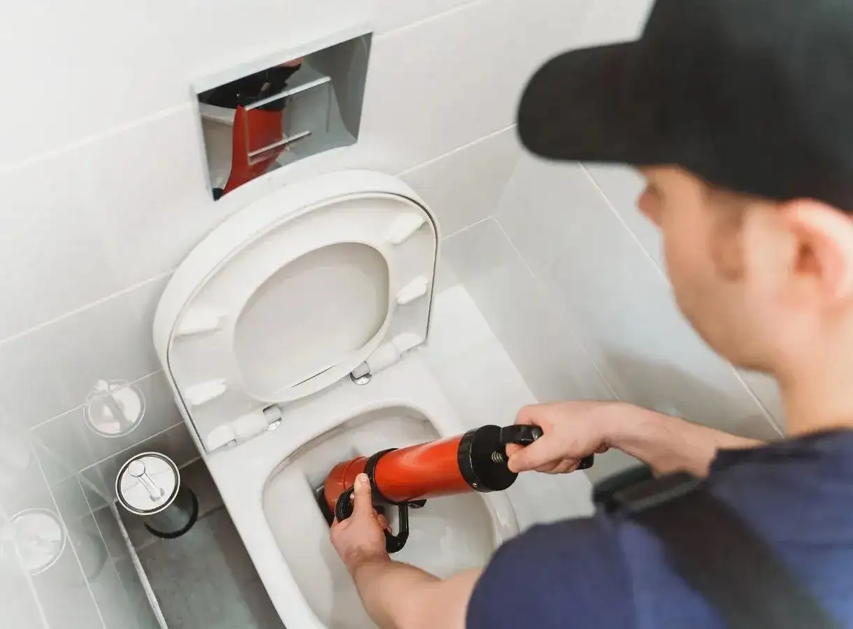 Un idraulico usa uno sturalavandini per liberare un WC bloccato. L'acqua gocciola, ma il problema verrà risolto presto.