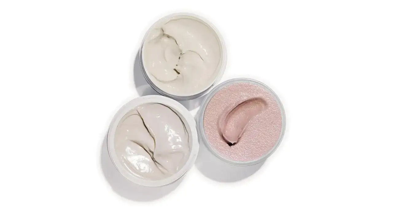 Tre barattoli aperti con texture cremose: un bianco avorio, un grigio chiaro e un rosa perlato. Ideali per un burro corpo nutriente.
