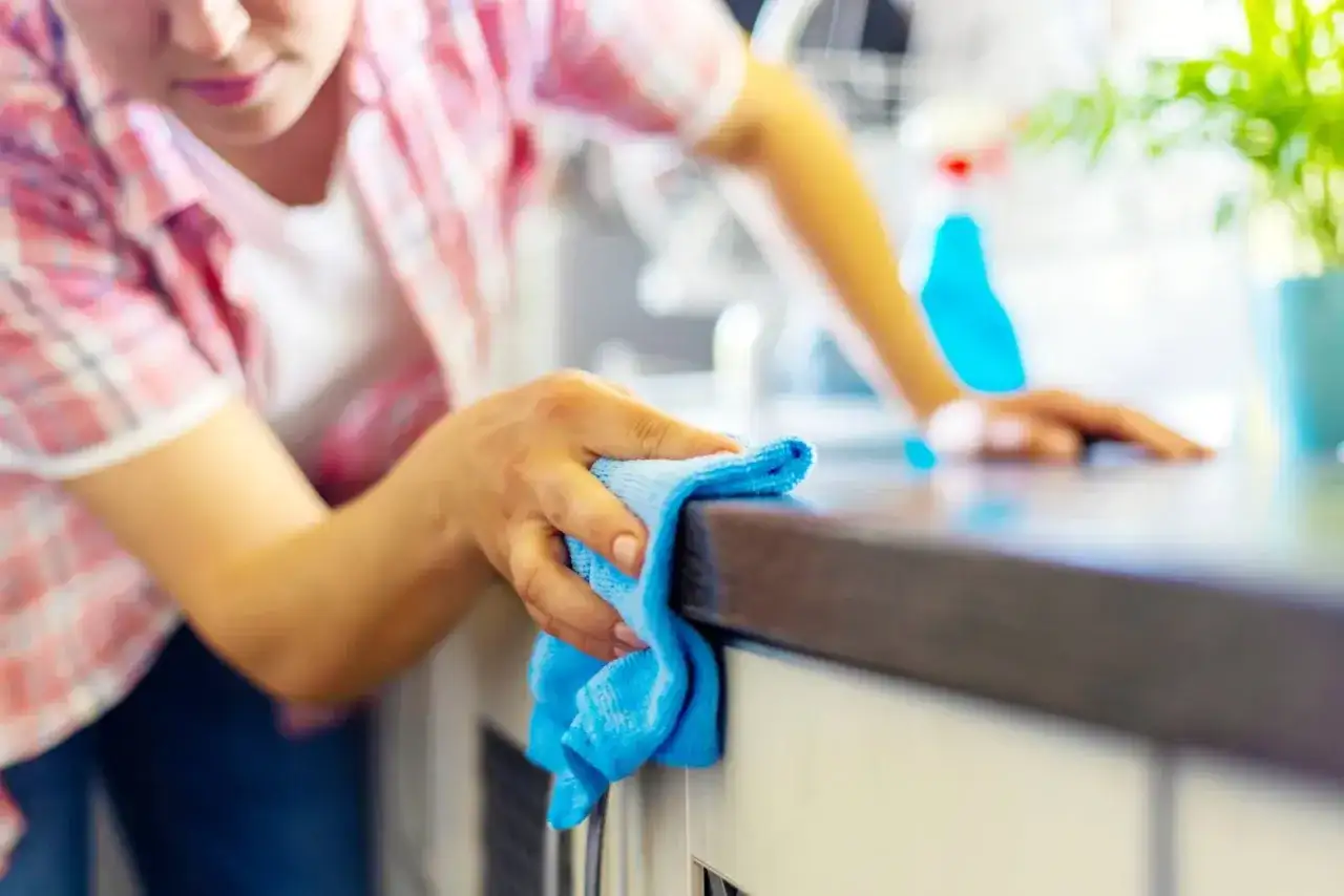 Donna pulisce il piano della cucina con un panno blu, un metodo efficace per sgrassare la cucina e mantenerla splendente.